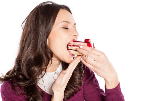 woman eating a slice of cake representing sugar cravings and hormonal appetite changes during menopause