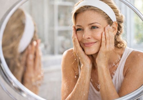 Woman over 40 with headband calming her skin after splashing cold water while looking in a mirror