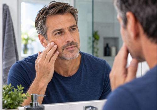 Man over 40 examining his skin in the bathroom mirror