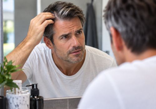 Middle-aged man examining gray hair at his temple in the bathroom mirror